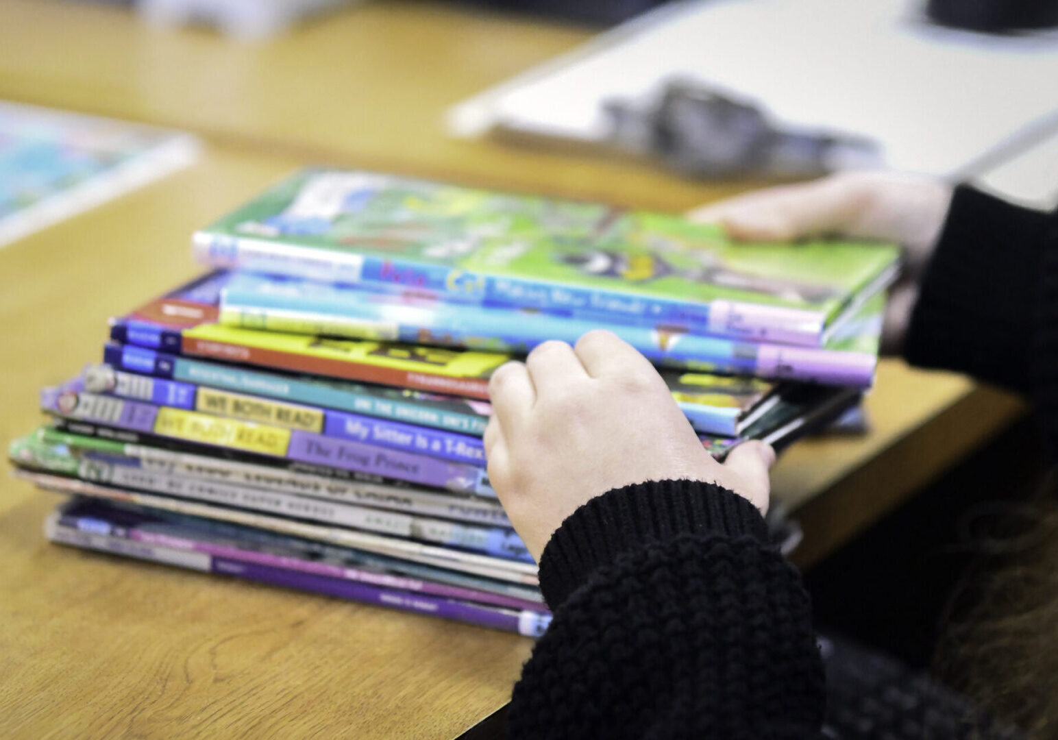 Faceless portrait of librarian sorting children's books A person holds a stack of colorful children's books on a wooden table.
