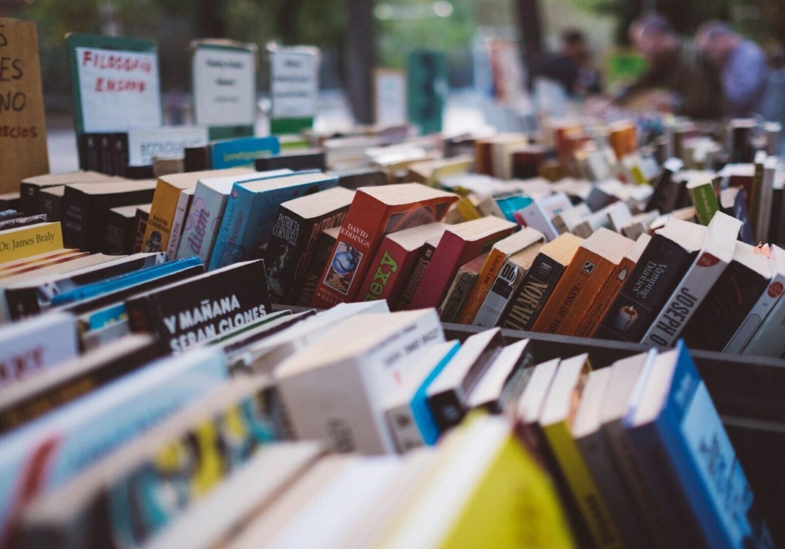 fm=f_103823 A display of assorted books, some stacked and others upright, at an outdoor market with people in the background.