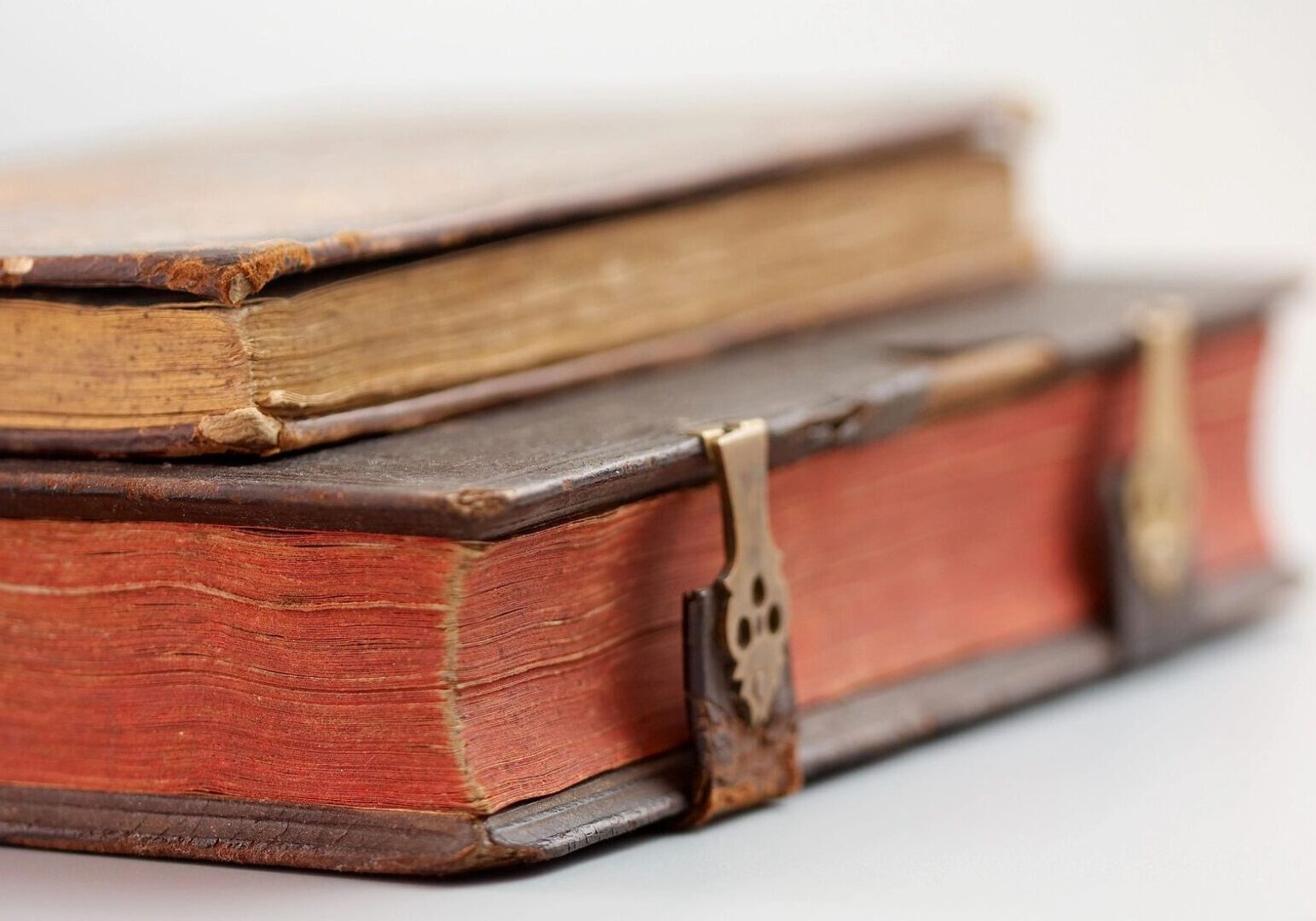 fm=f_115980 Two vintage books with worn edges. The top book has a visible spine and the bottom book features metal clasps.